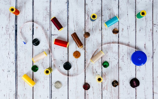 A detailed top-down shot of various materials laid out on a table for making a DIY dog collar: colorful nylon webbing, a sturdy plastic buckle, a metal D-ring, measuring tape, scissors, and thread.