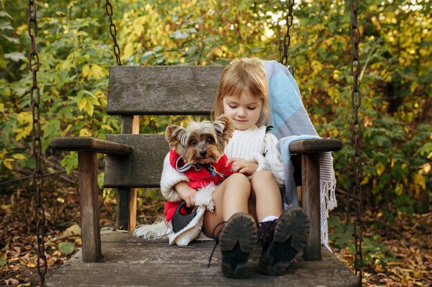 A small terrier puppy is gently being petted by a child while sitting on a park bench. The child is smiling, and the puppy appears calm and comfortable.
